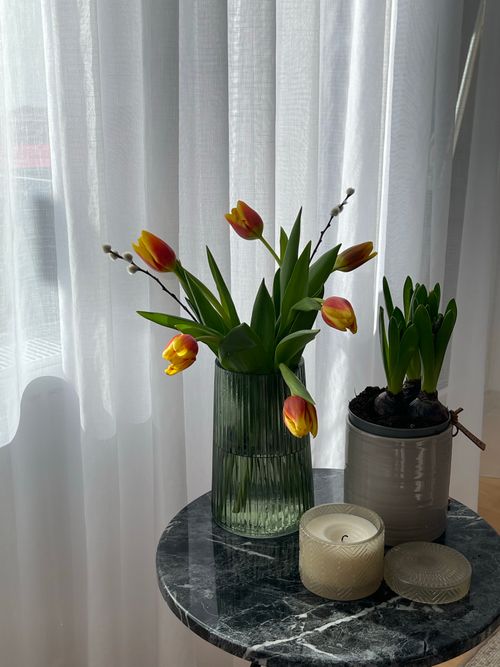 Free Bright tulips in a vase and candles on a marble table by soft curtains. Stock Photo
