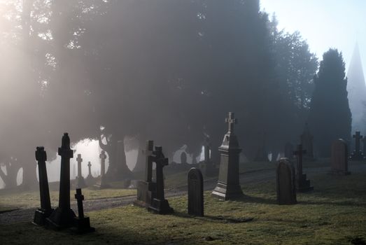 Misty morning scene in a historic graveyard in Penrith, England with towering gravestones and trees.