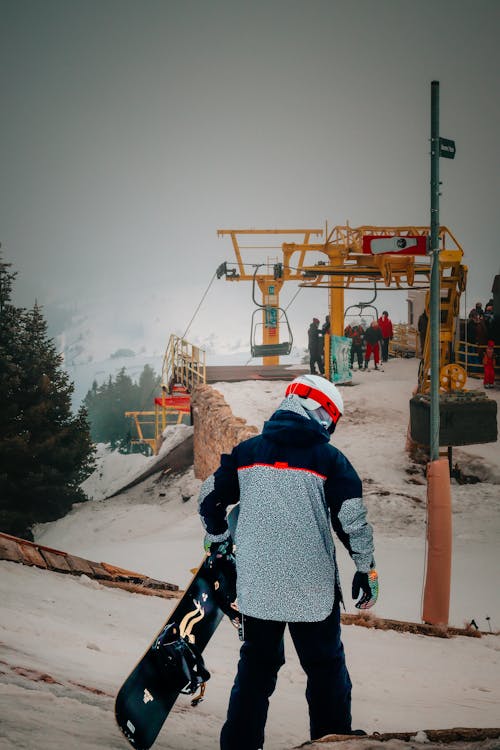 Back View of a Person with a Snowboard Walking on a Ski Slope 