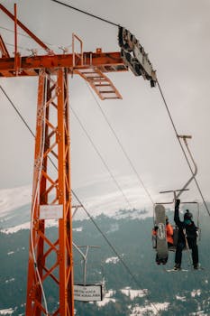 Two snowboarders ride a ski lift over a snowy mountain landscape, highlighting winter sports vibes.