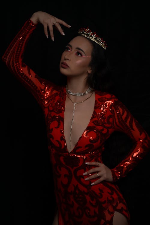 Young Woman in a Red Dress and a Tiara Posing with her Hand Raised 