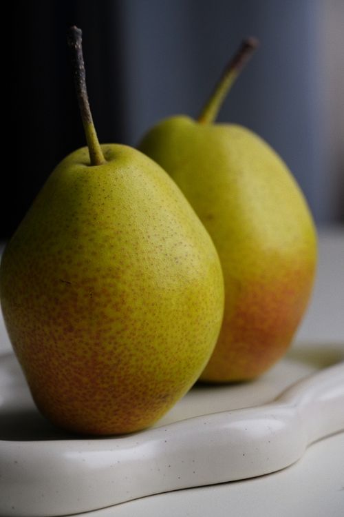 Free Intimate shot of two ripe pears on white ceramic tray with natural light, showcasing vibrant colors and textures. Stock Photo