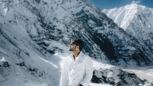 A man in white shirt standing in front of snowy mountains