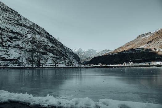 A peaceful winter scene featuring a frozen lake surrounded by snowy mountains.
