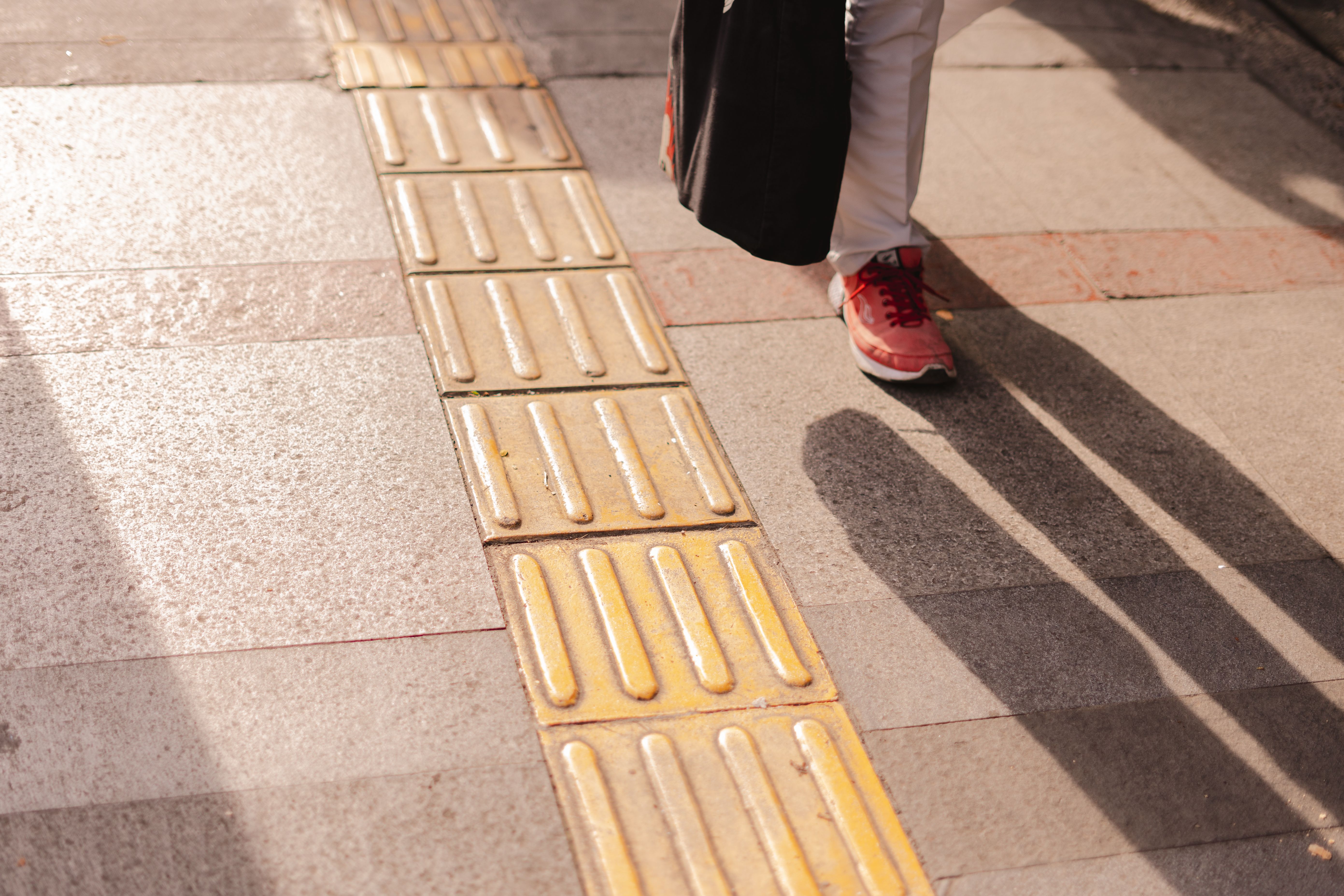 A sunlit urban sidewalk with textured tiles, casting long sh