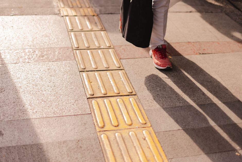 A sunlit urban sidewalk with textured tiles, casting long sh