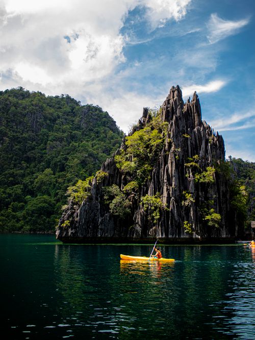 Free A lone kayaker navigates a serene bay with dramatic limestone cliffs and lush greenery. Stock Photo