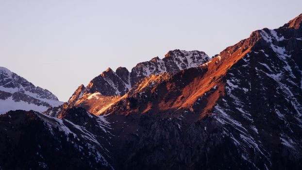 Stunning sunset view of snow-covered rocky peaks with warm golden light.