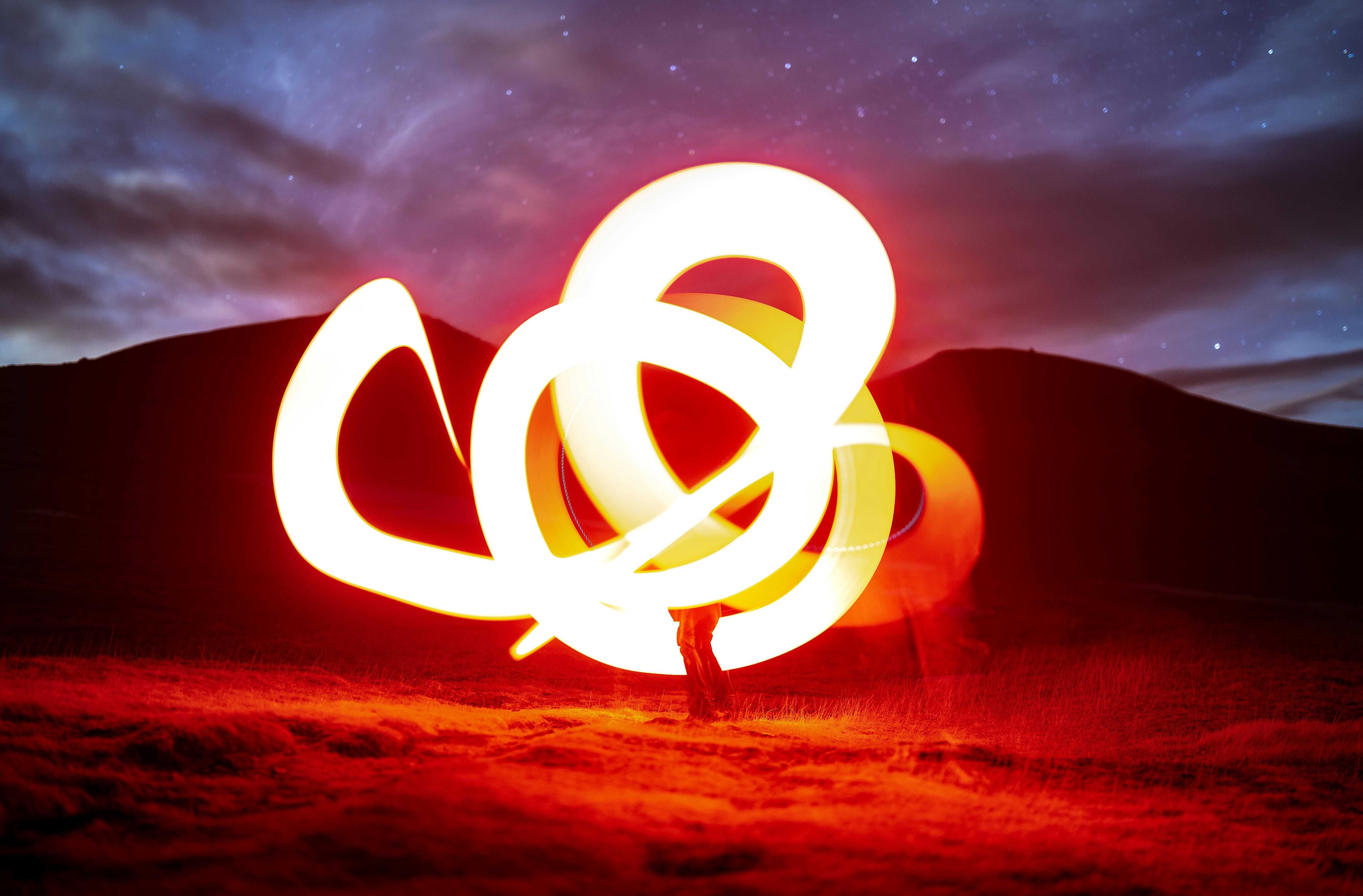 Bright and bold light painting illuminates a scenic mountain backdrop under a starlit night sky.