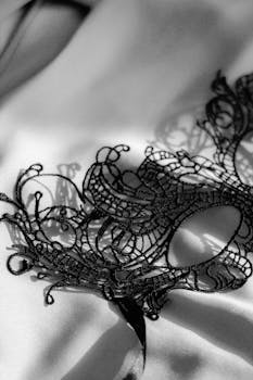 Close-up of an intricate black lace mask resting on smooth silk fabric, creating a mysterious and elegant atmosphere.