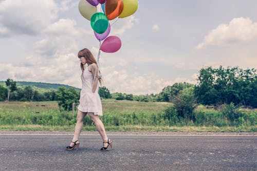 Photography of Woman Walking Near Road Holding Balloons