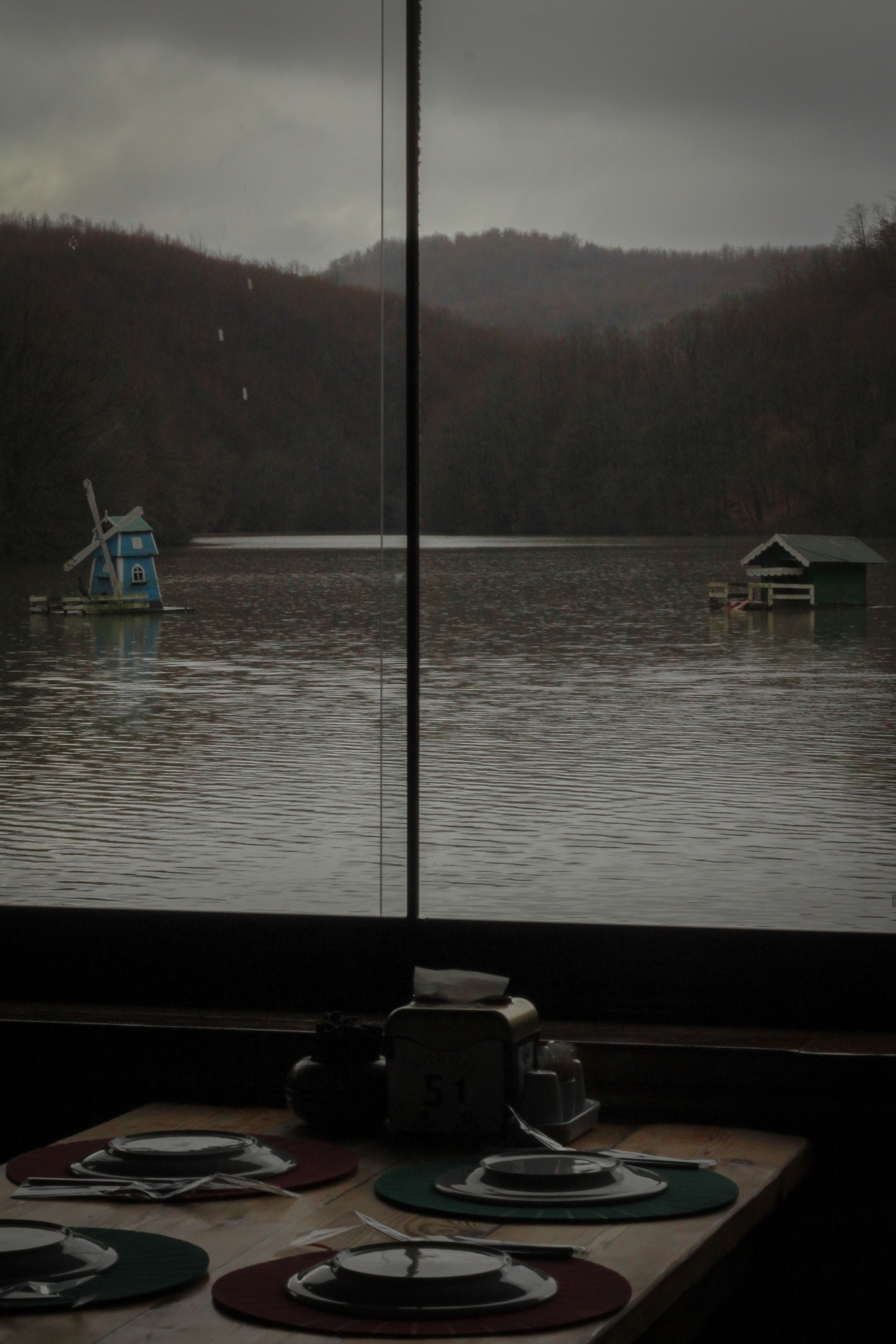 Serene view of a lake with windmill and sheds as seen from a restaurant window.
