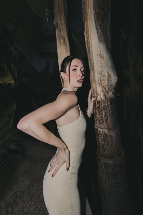 A woman in a white dress posing near a tree