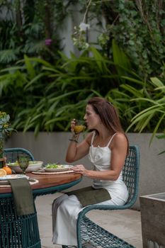 Woman enjoying a meal outdoors, sipping juice at a green-themed garden table.