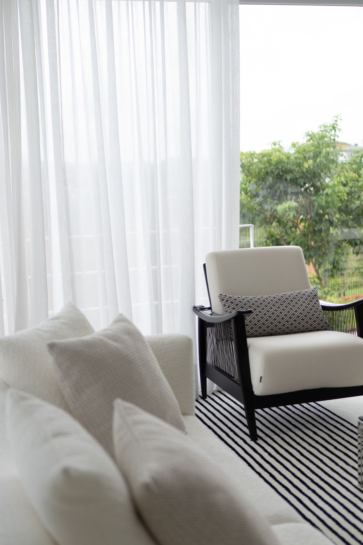 White sheer curtains beside a striped rug in a bright coastal room