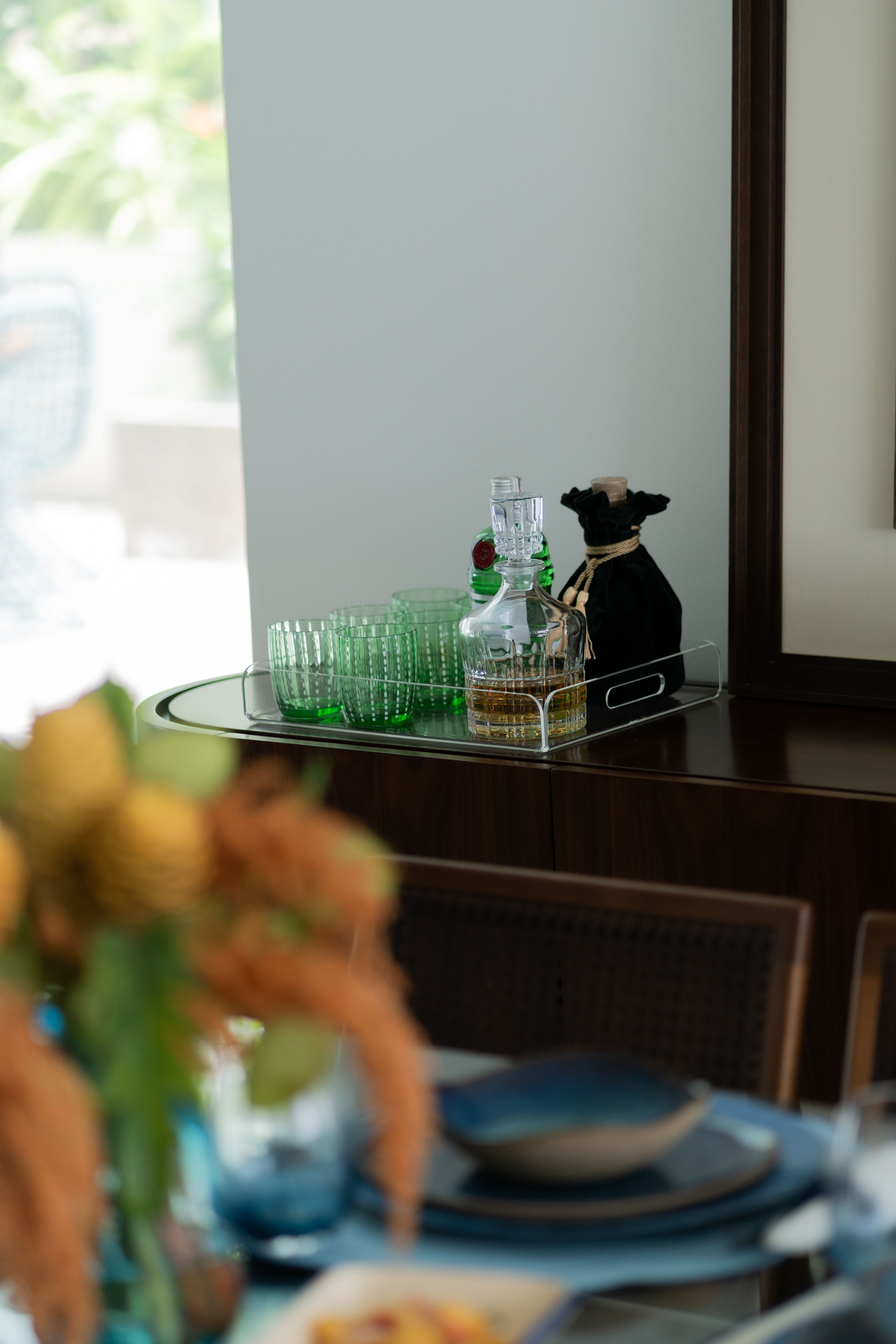 A stylish tray with green glassware and a bottle elegantly placed in a contemporary dining room setting.