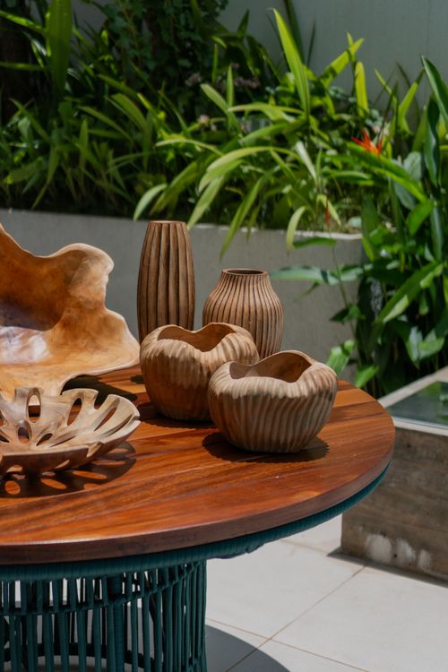 Free Beautifully carved wooden vases displayed on a patio table, surrounded by lush greenery. Stock Photo