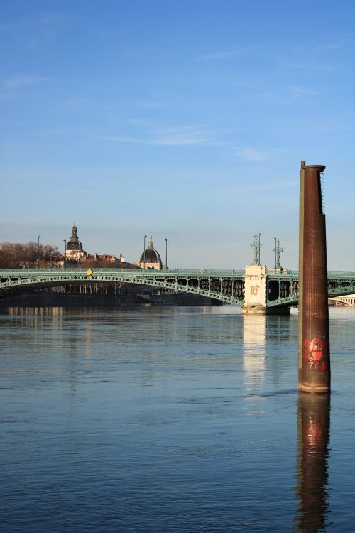 Free A scenic view of a metal bridge spanning a calm river under a clear blue sky. Stock Photo