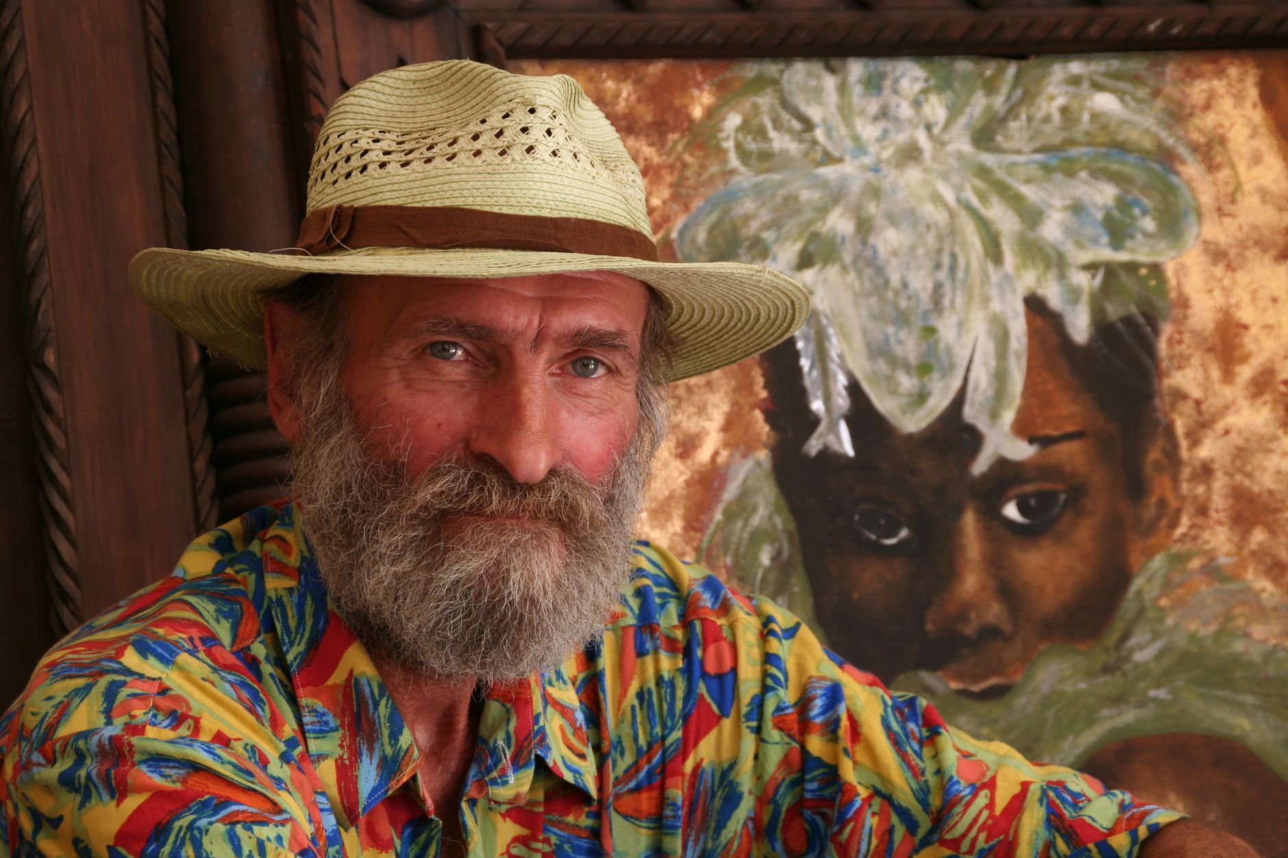 Bearded artist with hat posing in front of portrait painting in Marrakech.