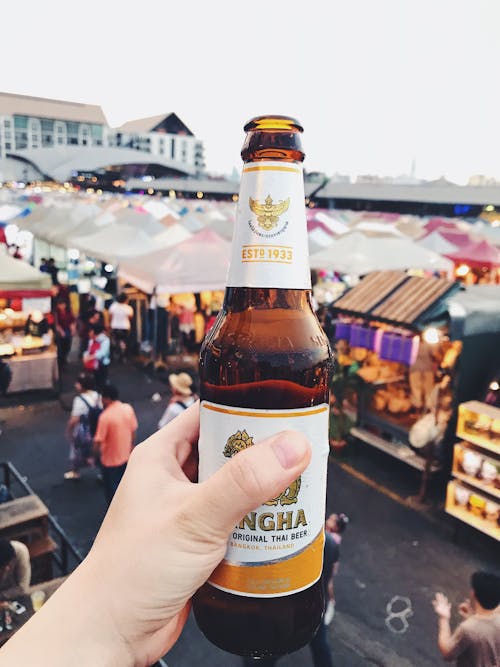 Person Holding White and Brown Labeled Bottle Overlooking Stalls