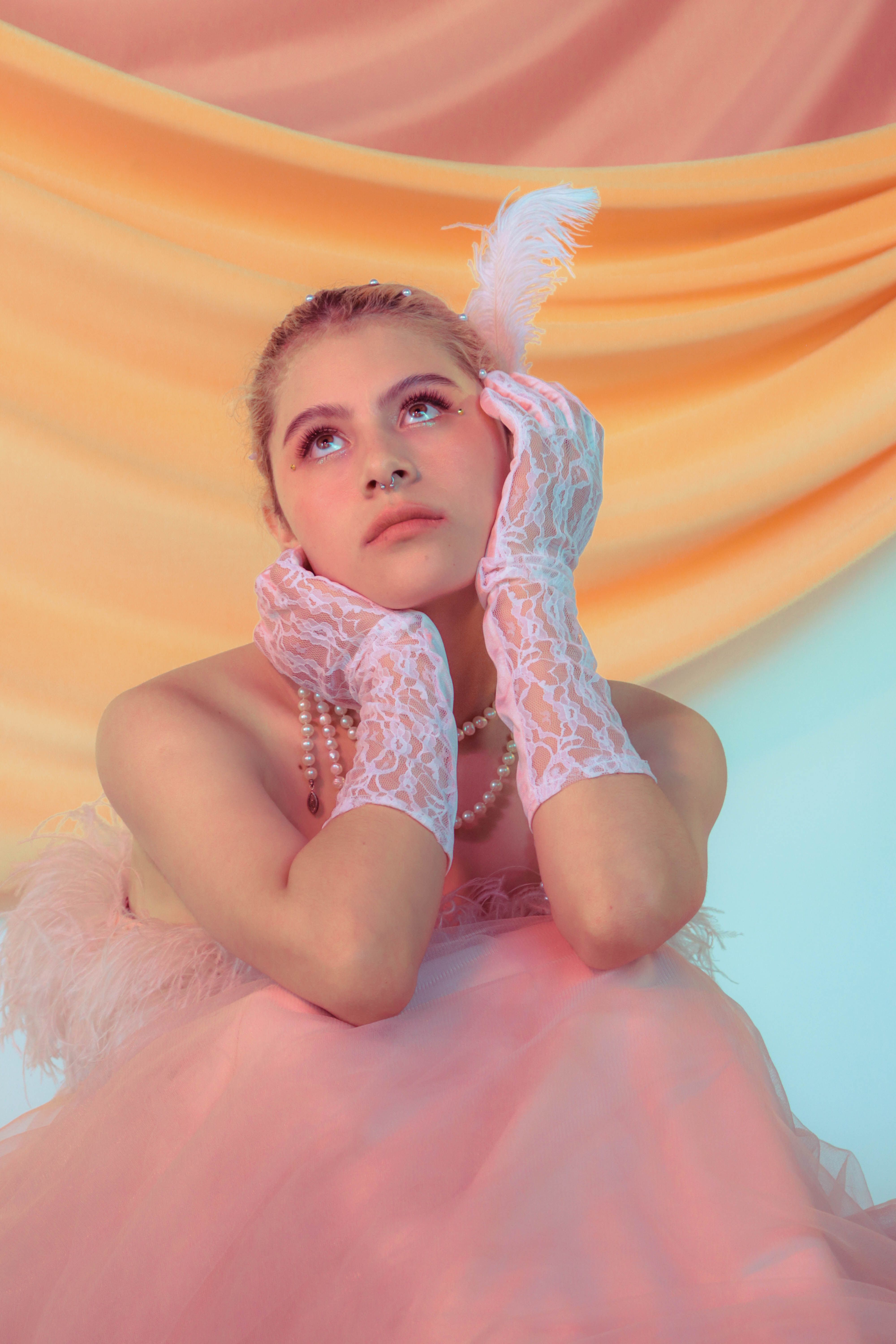 Elegant woman in retro fashion with lace gloves and pearls, looking up thoughtfully.