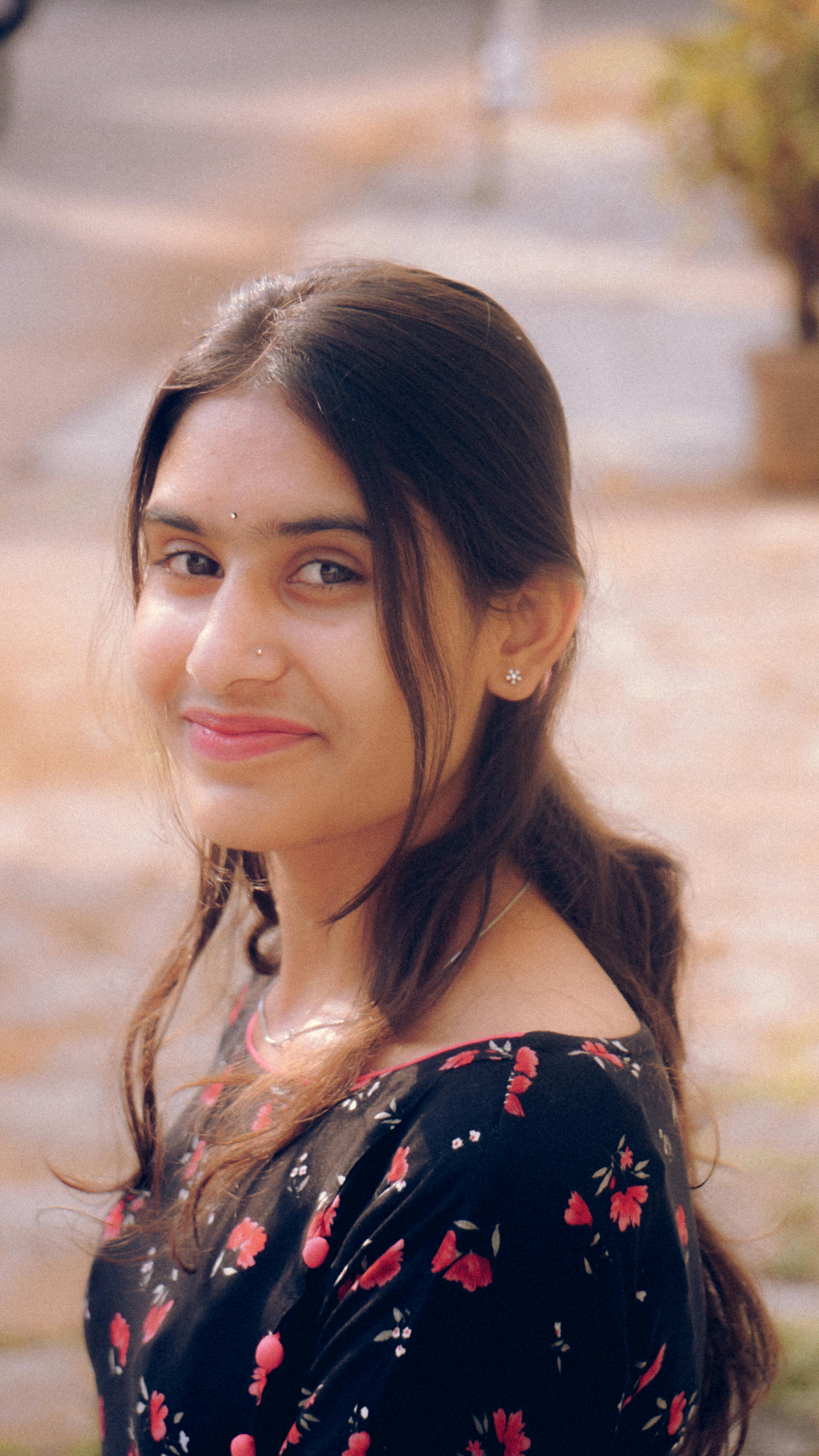 Charming portrait of a young woman smiling warmly, dressed in a floral outfit, outdoors.