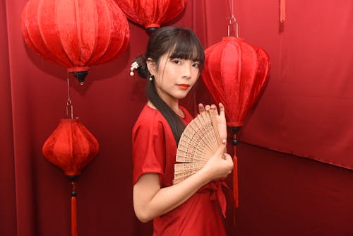 A woman in red holding a fan and some red lanterns