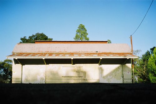 Free A weathered barn with a rusted roof stands alone under a clear blue sky in a rural setting. Stock Photo