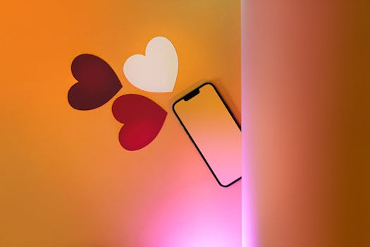 Flat lay of paper hearts and smartphone on orange background, perfect for Valentine's themes.