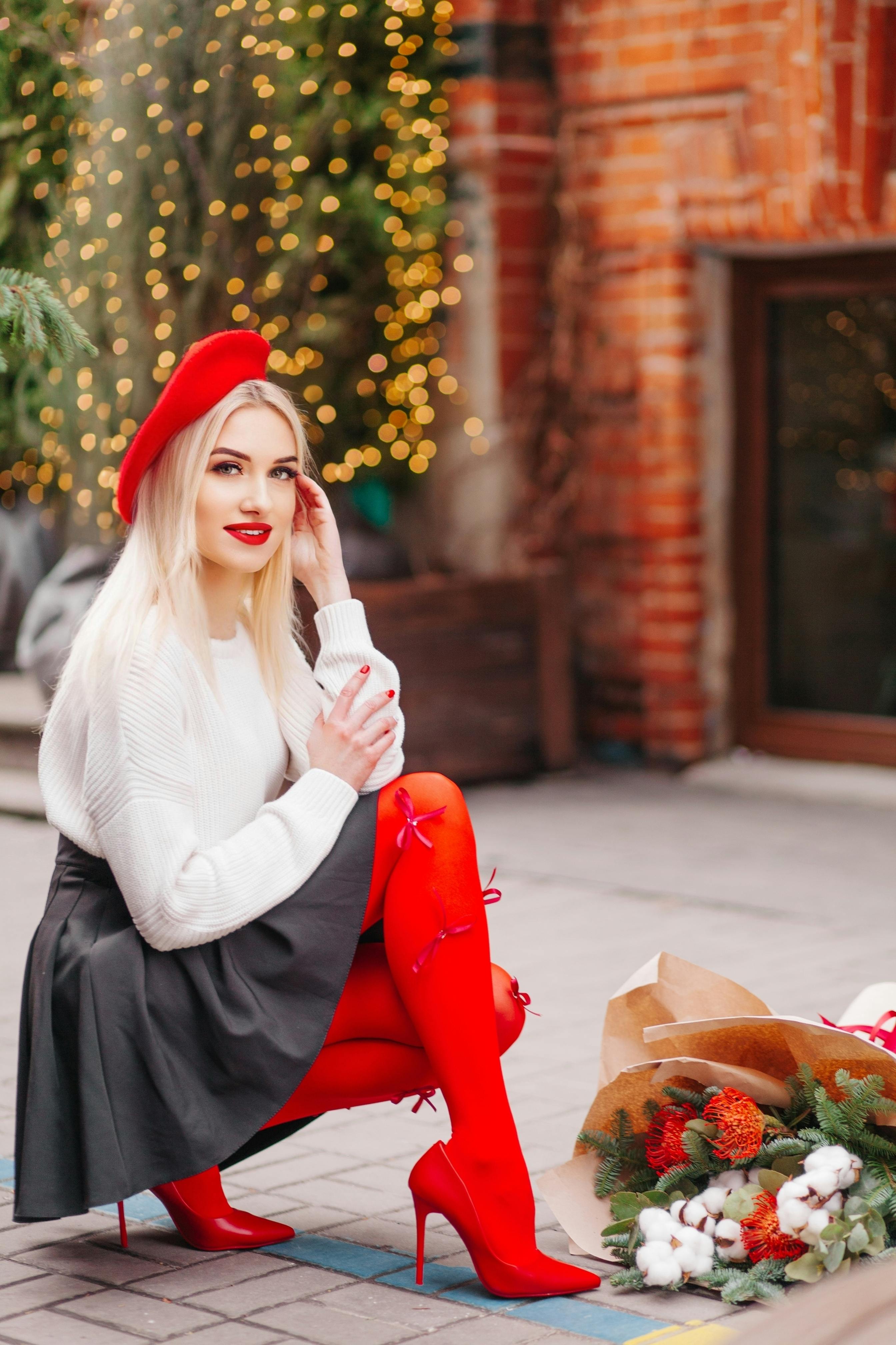 Elegant woman in red beret posing with festive bouquet on a city street, winter vibe.