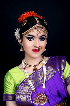 Captivating portrait of a woman in vibrant traditional attire adorned with elaborate jewelry against a dark backdrop.