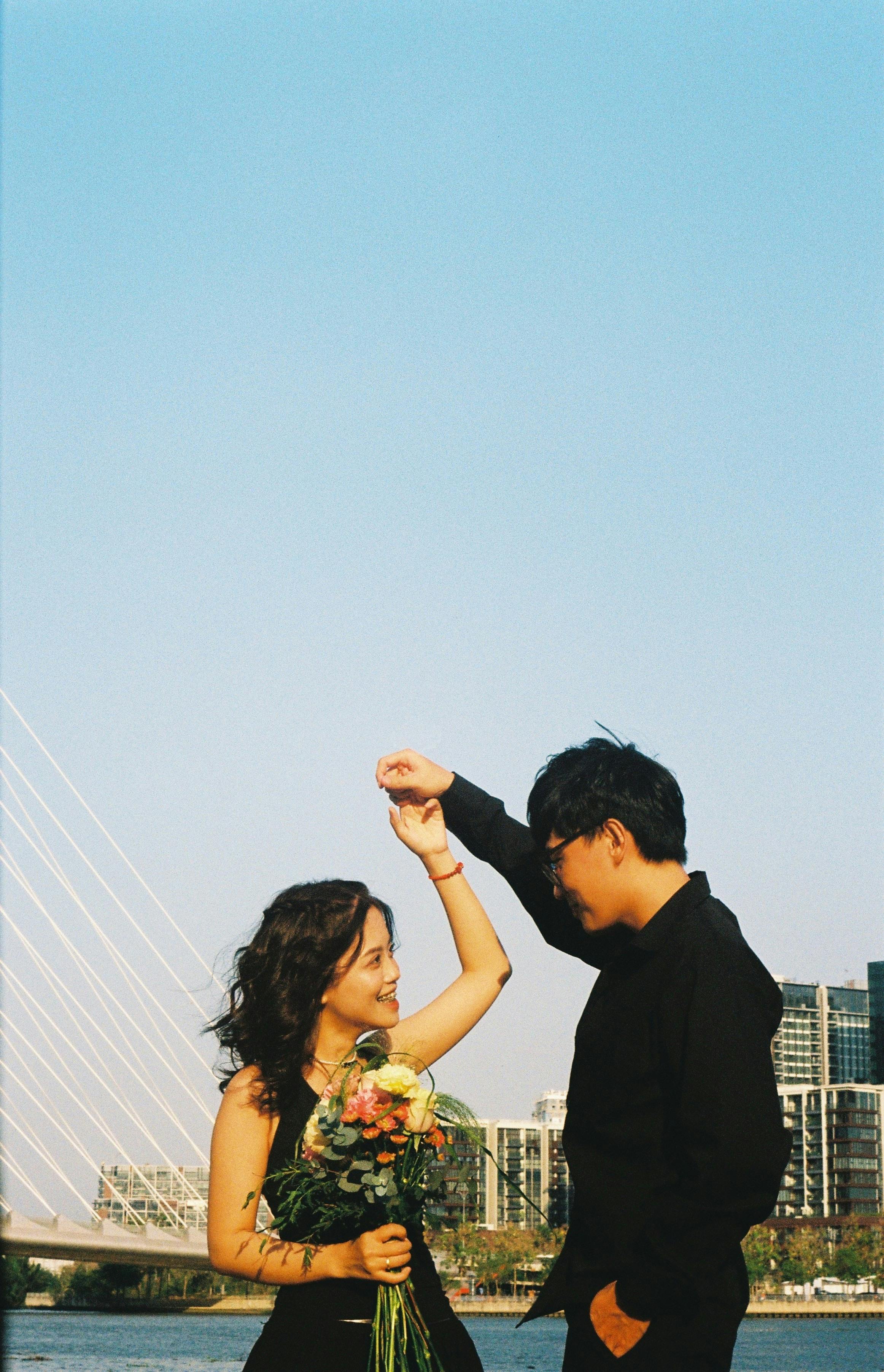 A joyful couple dances outdoors, holding a bouquet, showcasing love and happiness.