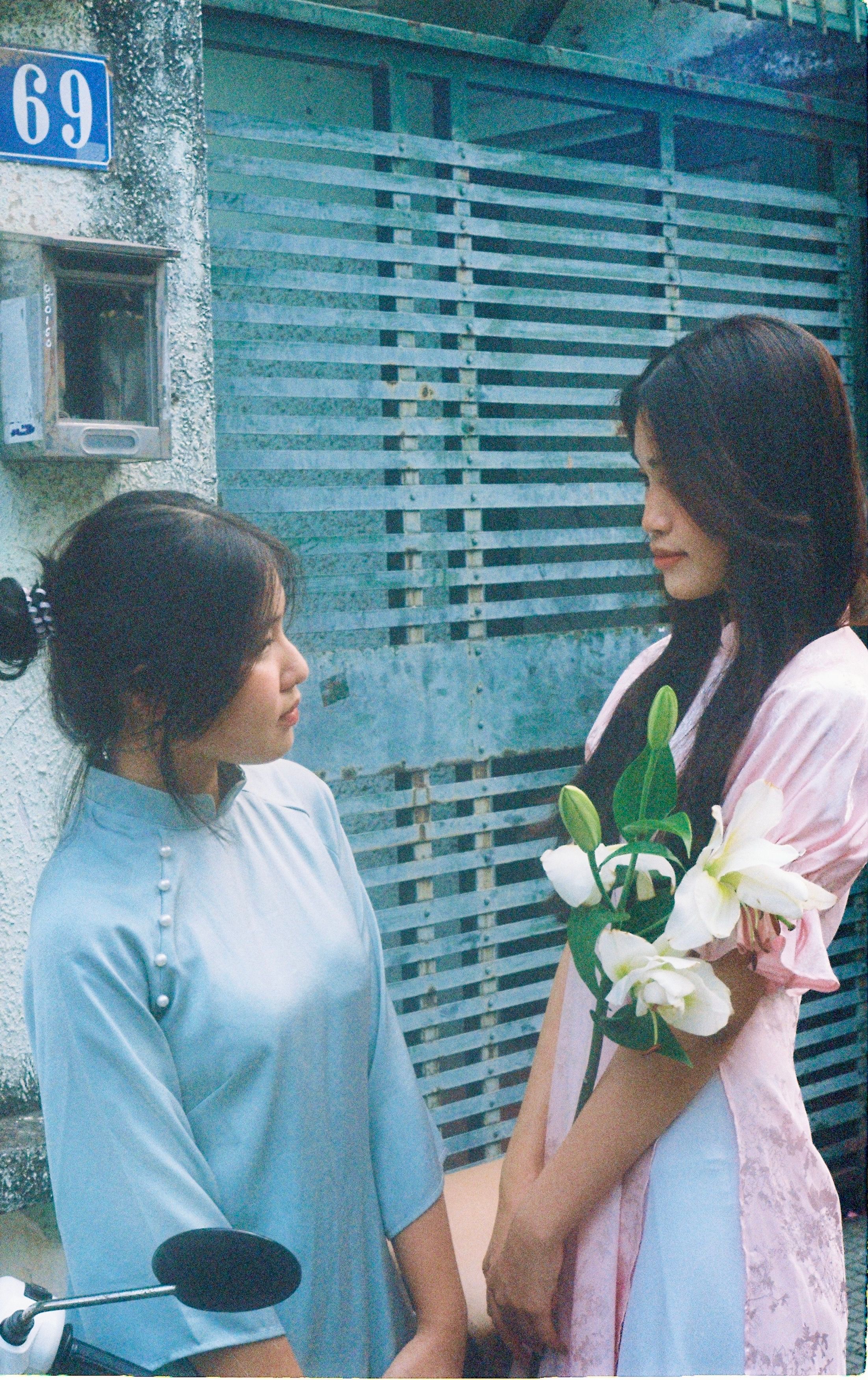 Two young women in traditional ao dai with lilies outdoors in Vietnam.
