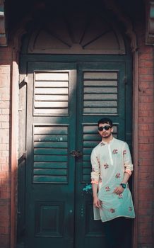 A fashionable man in traditional attire poses against an antique wooden door. Urban setting, stylish image.