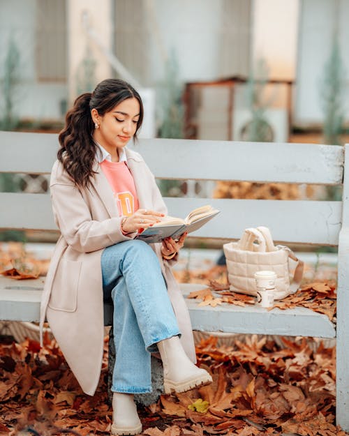 Young Woman Sitting on a Bench with a Book and Coffee