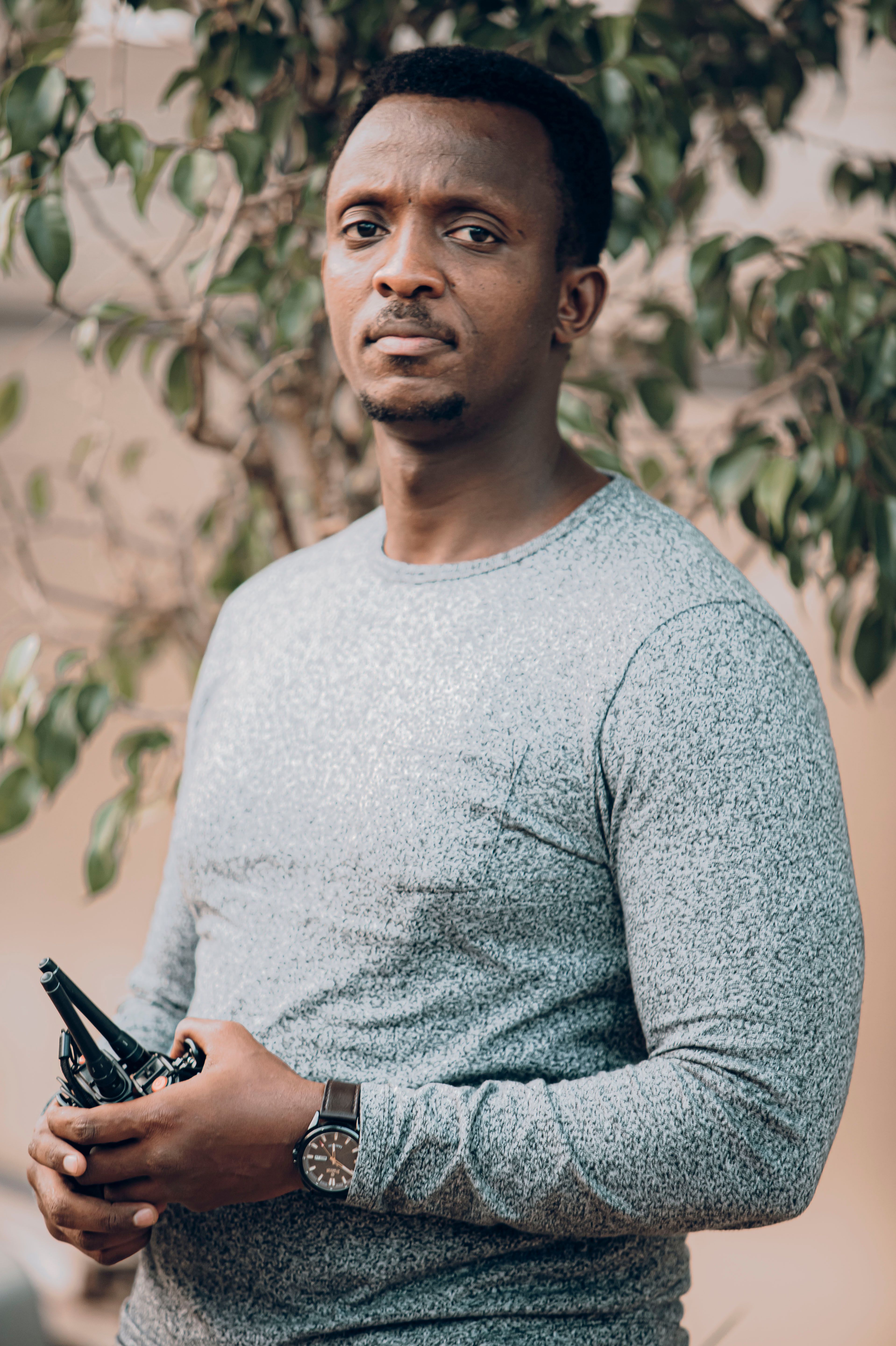 A confident man with a wristwatch standing outdoors, wearing a casual gray sweater.