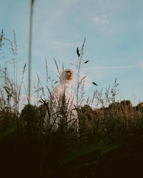 A woman in a hijab peacefully standing in a picturesque rural field under a clear sky.