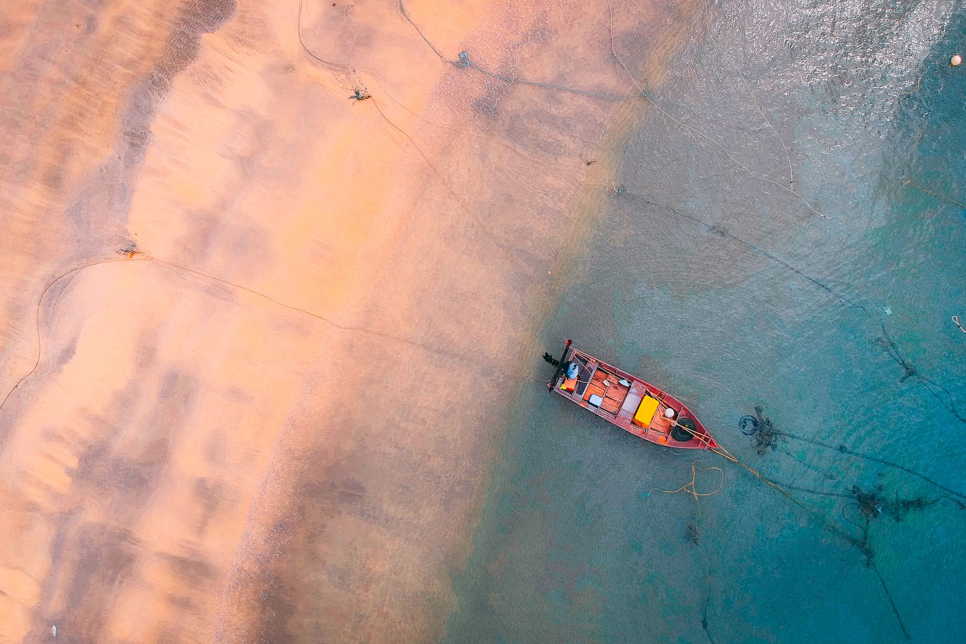 A drone captures a solitary boat anchored near a serene beach shore, surrounded by turquoise waters.
