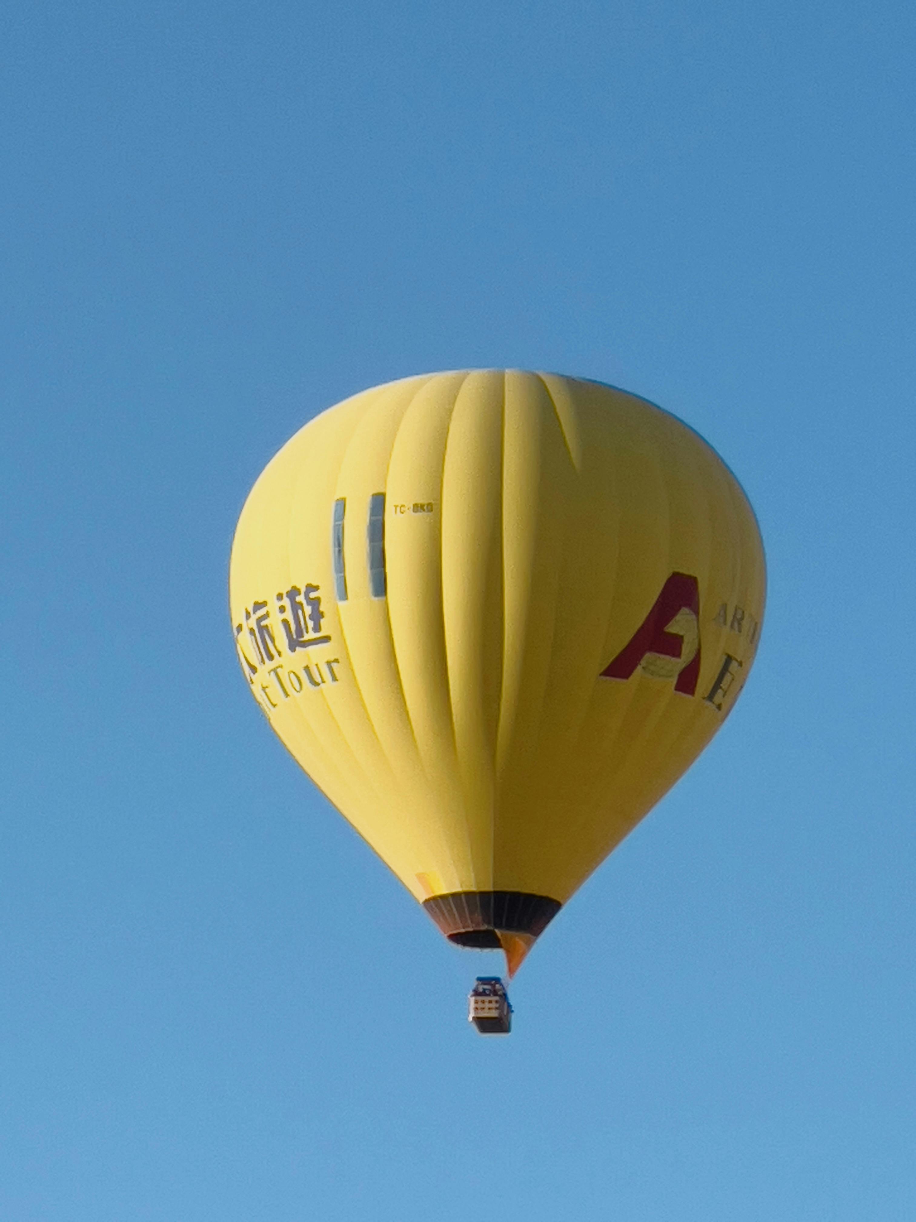 A vibrant yellow hot air balloon soars against a clear blue sky, perfect for adventure seekers.