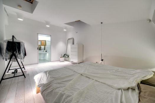 A modern minimalist bedroom featuring white decor, a cozy bed, and a stylish clothes rack.
