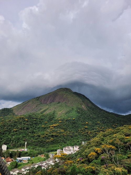 Free Aerial view of a lush green mountain under dramatic clouds over a small village. Stock Photo