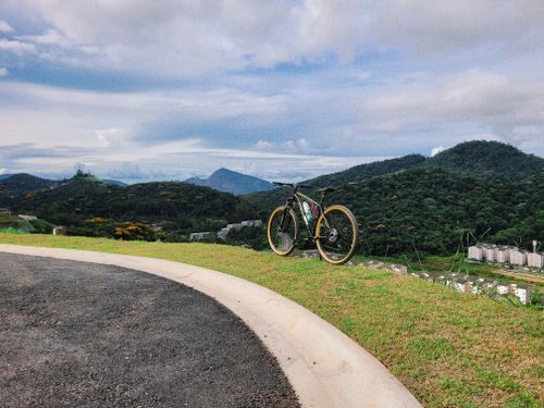 Free A scenic view of a bicycle on a mountain trail with a lush green forest and cloudy sky. Stock Photo