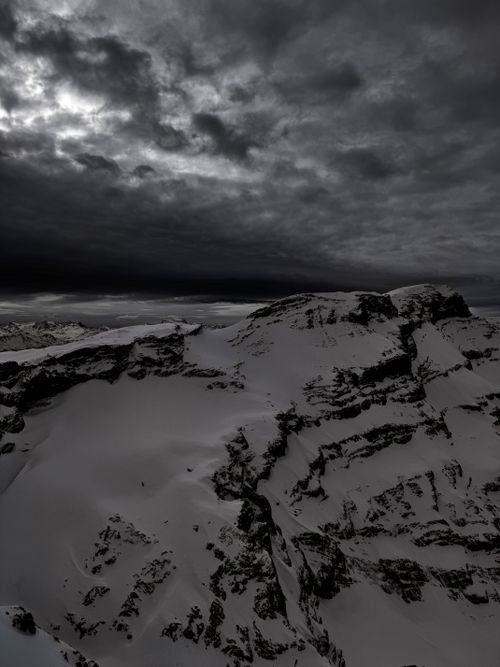 Free Aerial view of snow-covered mountains in Switzerland, beneath dark, dramatic clouds. Stock Photo