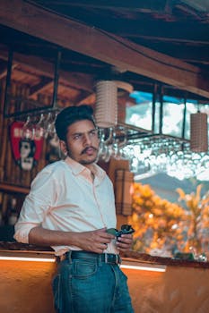 乡村酒吧里，一名时尚男子戴着墨镜，若有所思地靠在吧台边，气氛温暖而轻松