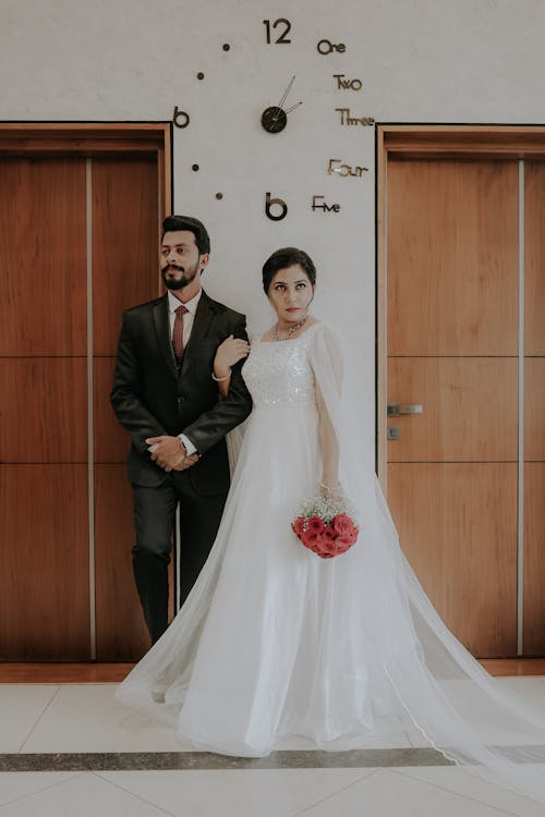 A bride and groom standing in front of a clock