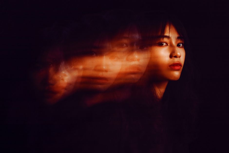 Creative double exposure portrait with an East Asian woman in focus against a dark background.