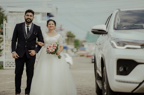 A bride and groom standing next to a car