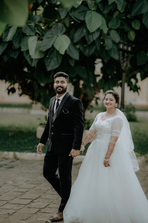 A bride and groom walking together in front of a tree