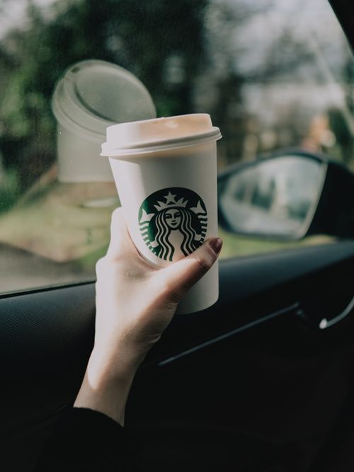 Free A hand holding a coffee cup inside a car, symbolizing a cozy morning commute. Stock Photo