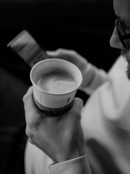 A man in monochrome holding a coffee cup and smartphone, captured in black and white.. monochrome, holding, coffee